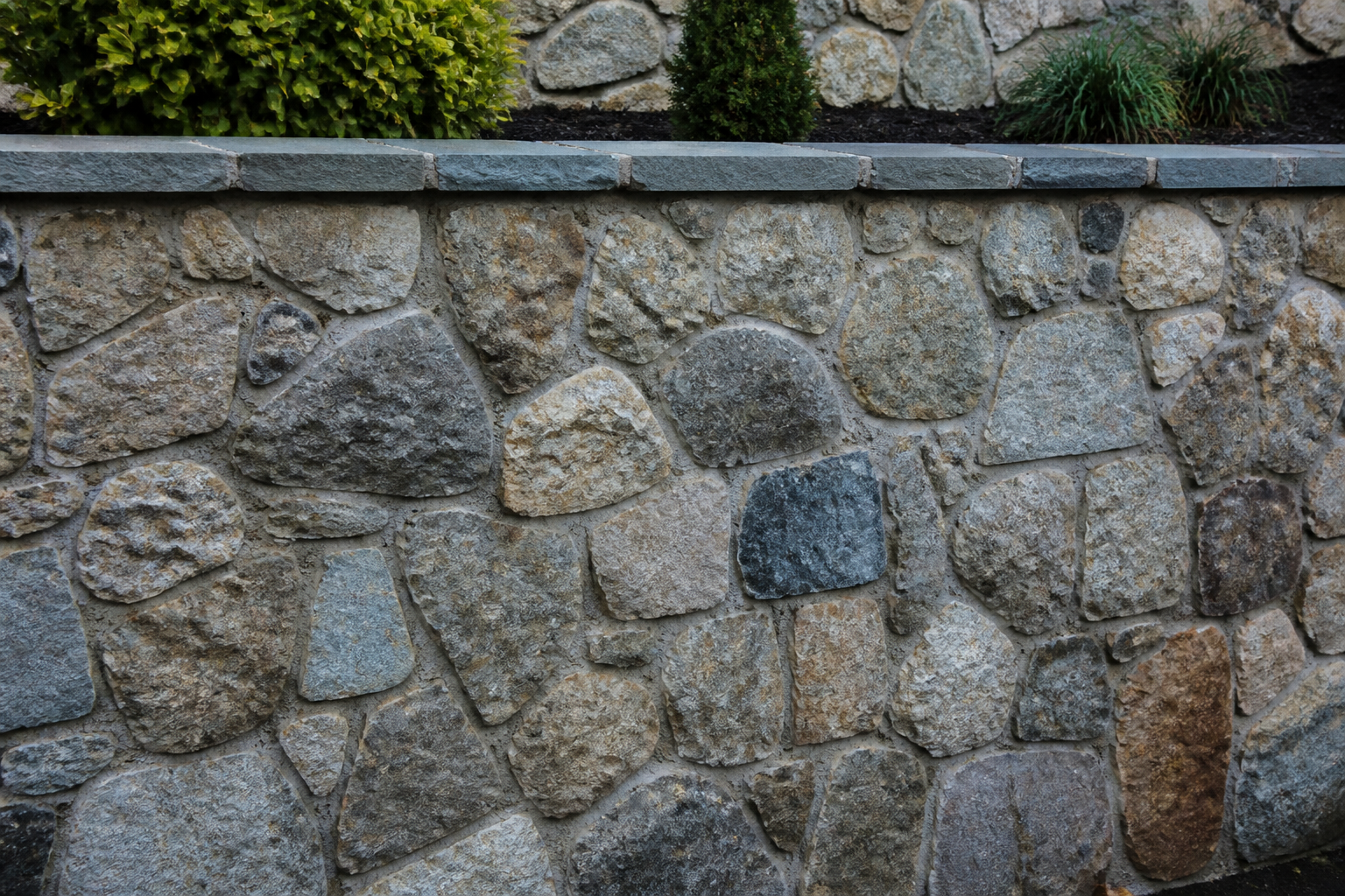 Natural stone retaining wall face with cap stones retaining a grade change — representative design concept