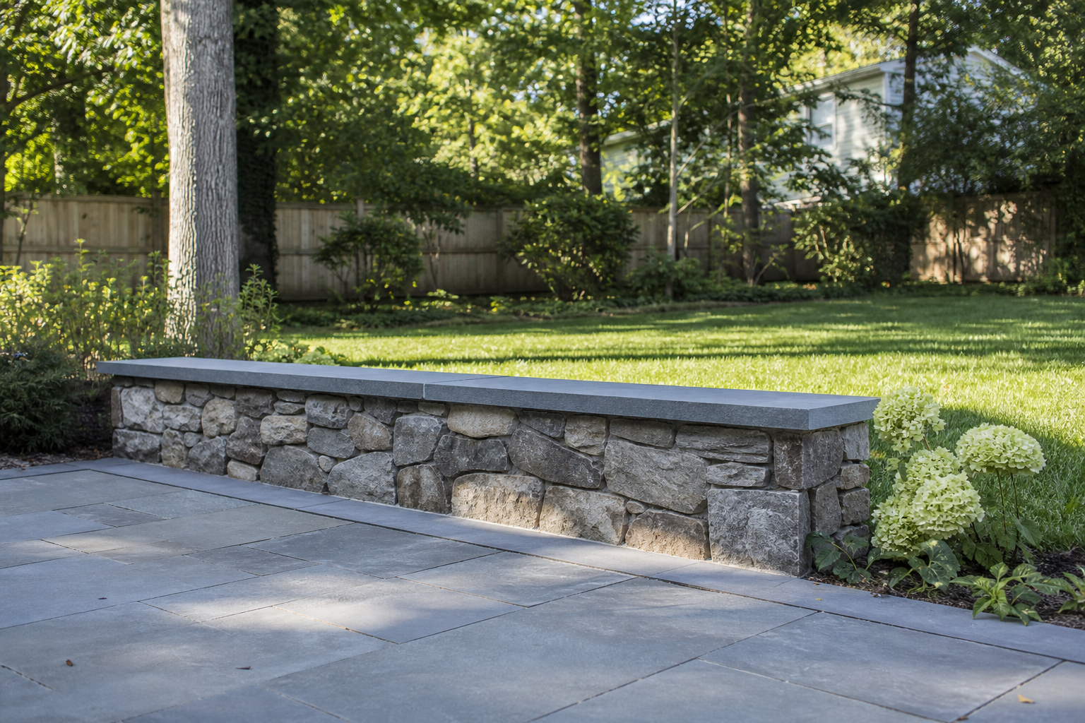 Low natural stone seat wall with bluestone cap on a bluestone patio in a landscaped backyard — representative design concept
