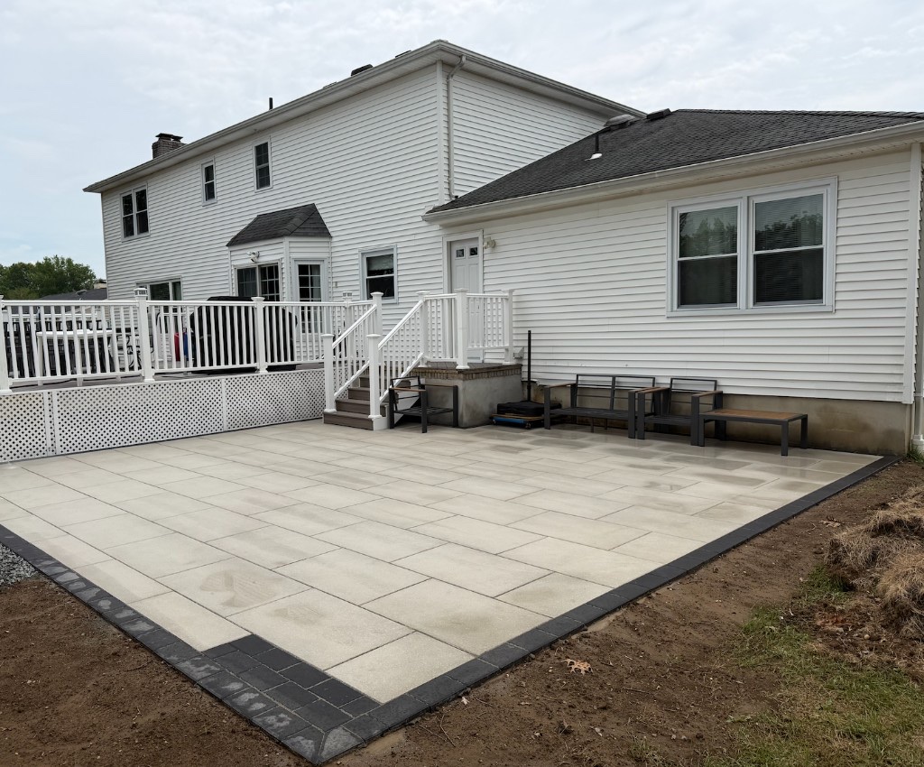 Completed rectangular paver patio with charcoal border beside a white elevated deck in Northern New Jersey
