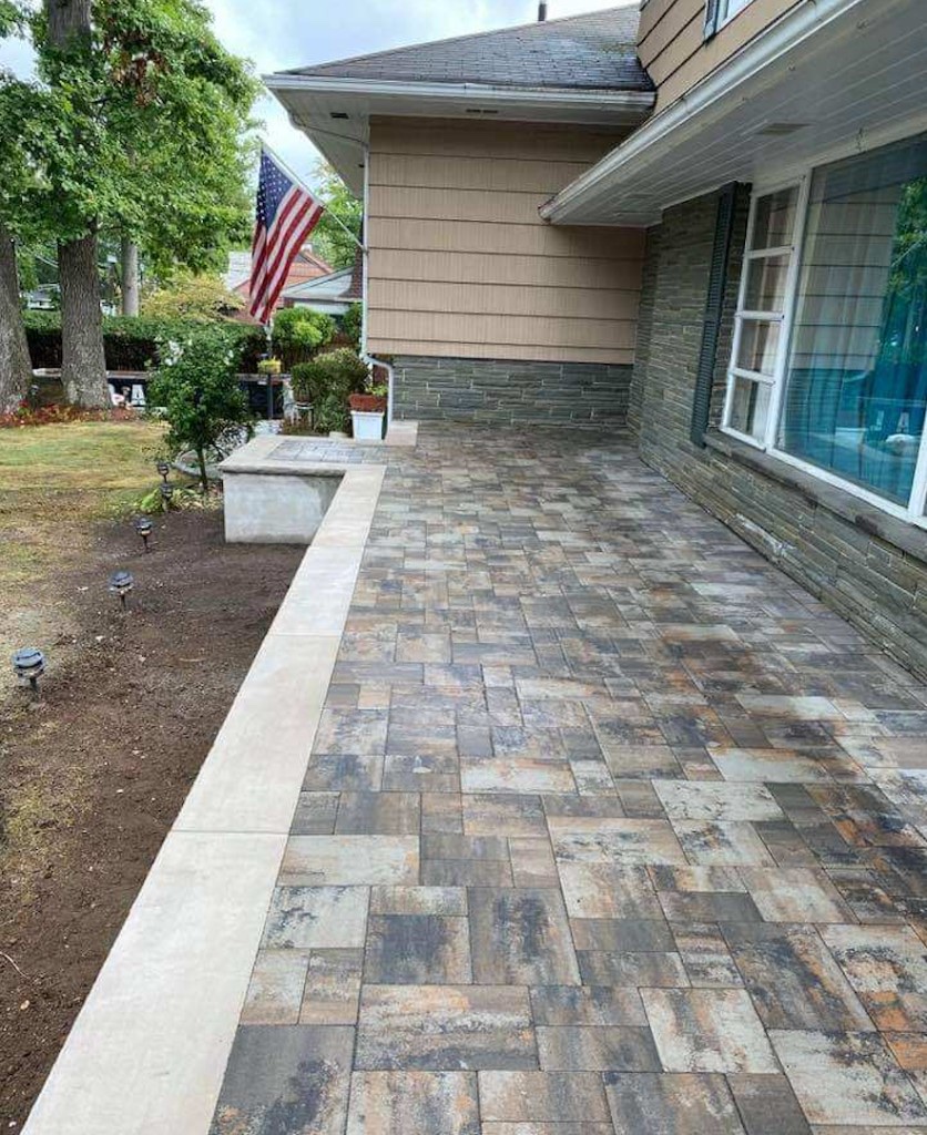 Completed elevated paver patio with light stone coping along a home exterior in Northern New Jersey