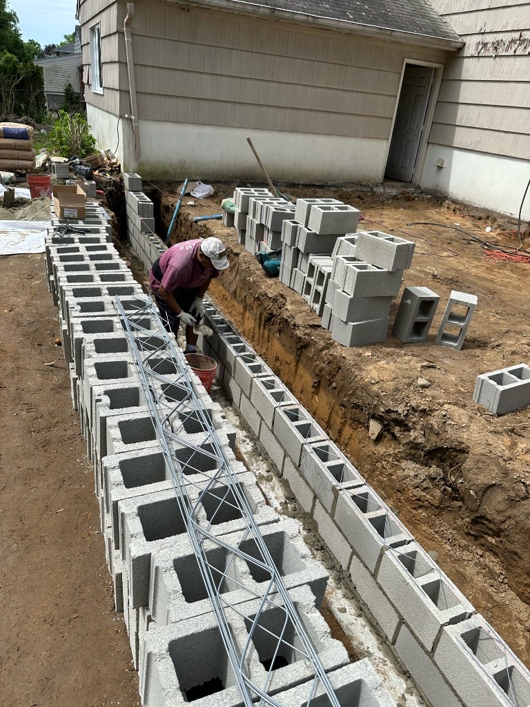 Worker laying cinder blocks in a trench beside a home foundation in Northern New Jersey